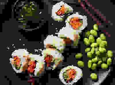 Image of some veggie sushi rolls with avocado and Edamamé beans on a black plate