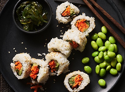 Image of some veggie sushi rolls with avocado and Edamamé beans on a black plate